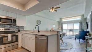 A modern kitchen with stainless steel appliances, a central island with a sink, and a dining area with a view of the balcony.