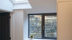 A room with a skylight, a window with a stone wall view, a wooden dresser, and a door. - 🌿 Countryside Escape – Chic Tiny Home in the Heart of the Cotswolds (Blockley)