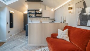 A modern kitchen with a central island, pendant lighting, and a red sofa in a living area. - Chic Cotswold Tiny Home - Oddity House (Blockley)