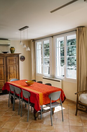 A dining area with a table covered in a red tablecloth, surrounded by chairs, and a window with curtains. - Villa Balleti - private pool with a view (Apt)