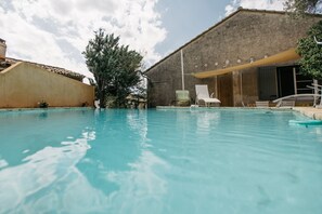 A swimming pool with lounge chairs and a building with a textured facade. - Villa Balleti - private pool with a view (Apt)