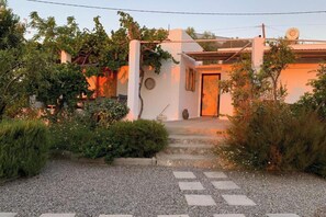 Ein Haus mit einem Schotterweg, der zu einer Holztür führt, umgeben von Grünpflanzen und einer Pergola.