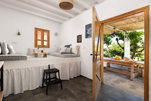 A room with a bed, a small table, a chair, a window, and a door leading outside.
