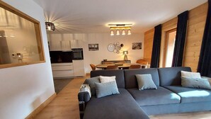 A modern living room with a grey sofa, wooden flooring, and a dining area in the background.