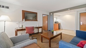 A modern living room with a sofa, a coffee table, a desk with a lamp, a television, and a kitchenette with a microwave. - 315@Loso Hotel (Charlotte)