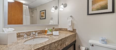 A bathroom with a granite countertop, sink, mirror, towel rack, toilet, and a framed picture on the wall.