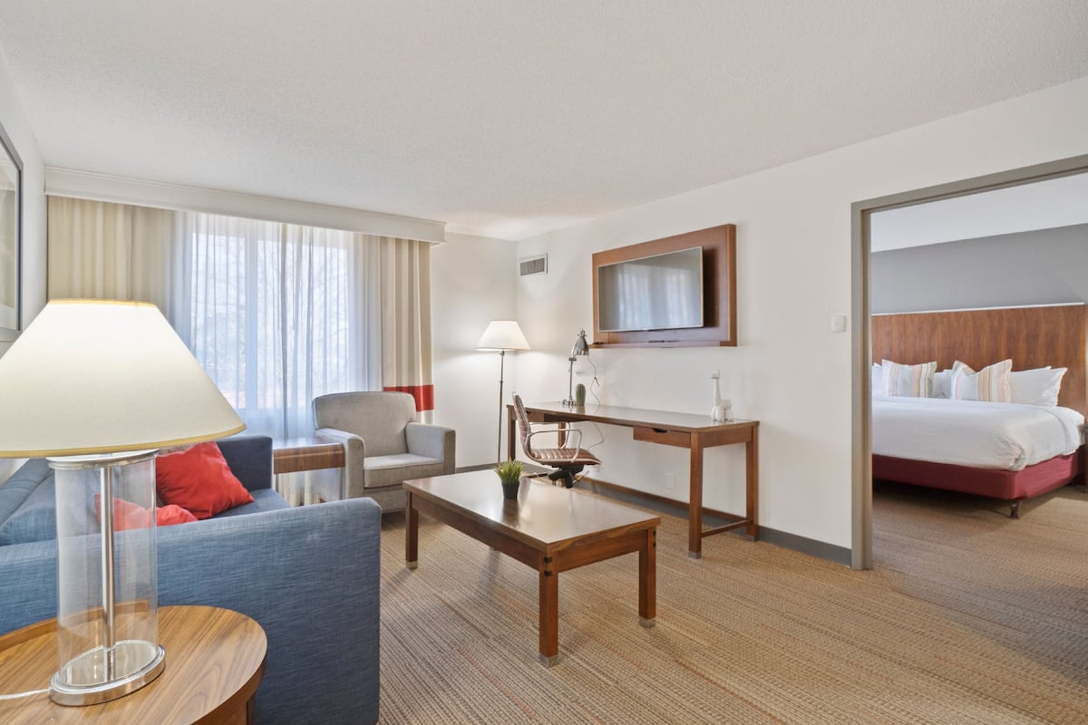 A hotel room with a sofa, a desk, a chair, a bed, and a TV.