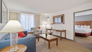 A hotel room with a sofa, a desk, a chair, a bed, and a TV.
