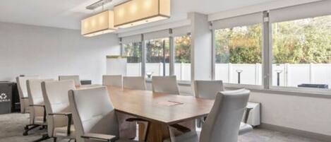 A conference room with a large table, several chairs, and large windows providing a view of the outdoors.