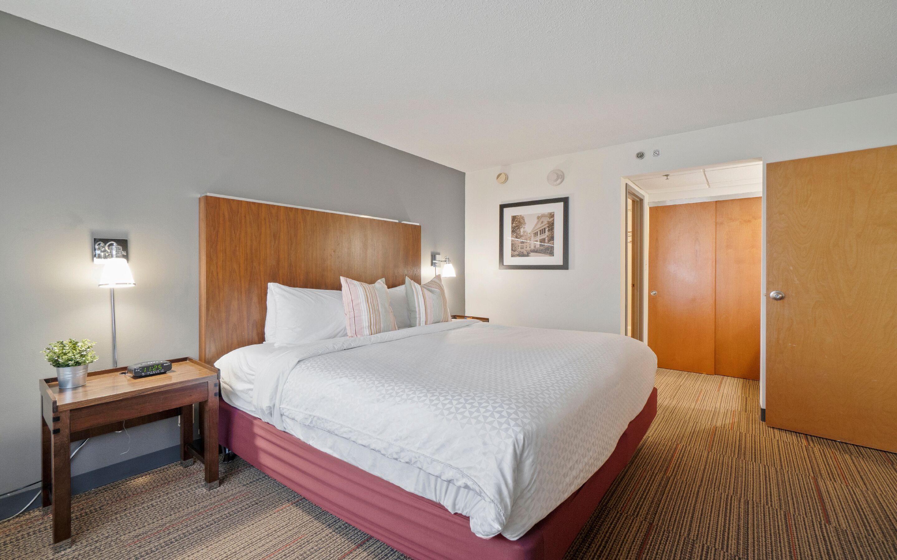 A hotel room with a bed, bedside table, lamp, and a framed picture on the wall.
