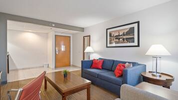 Een moderne hotelkamer met een blauwe bank, rode kussens, een houten salontafel en een lijst met een stadsbeeld aan de muur.