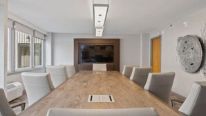 A conference room with a long wooden table, white chairs, a flat-screen TV, and a unique wall decoration. - 315@Loso Hotel (Charlotte)
