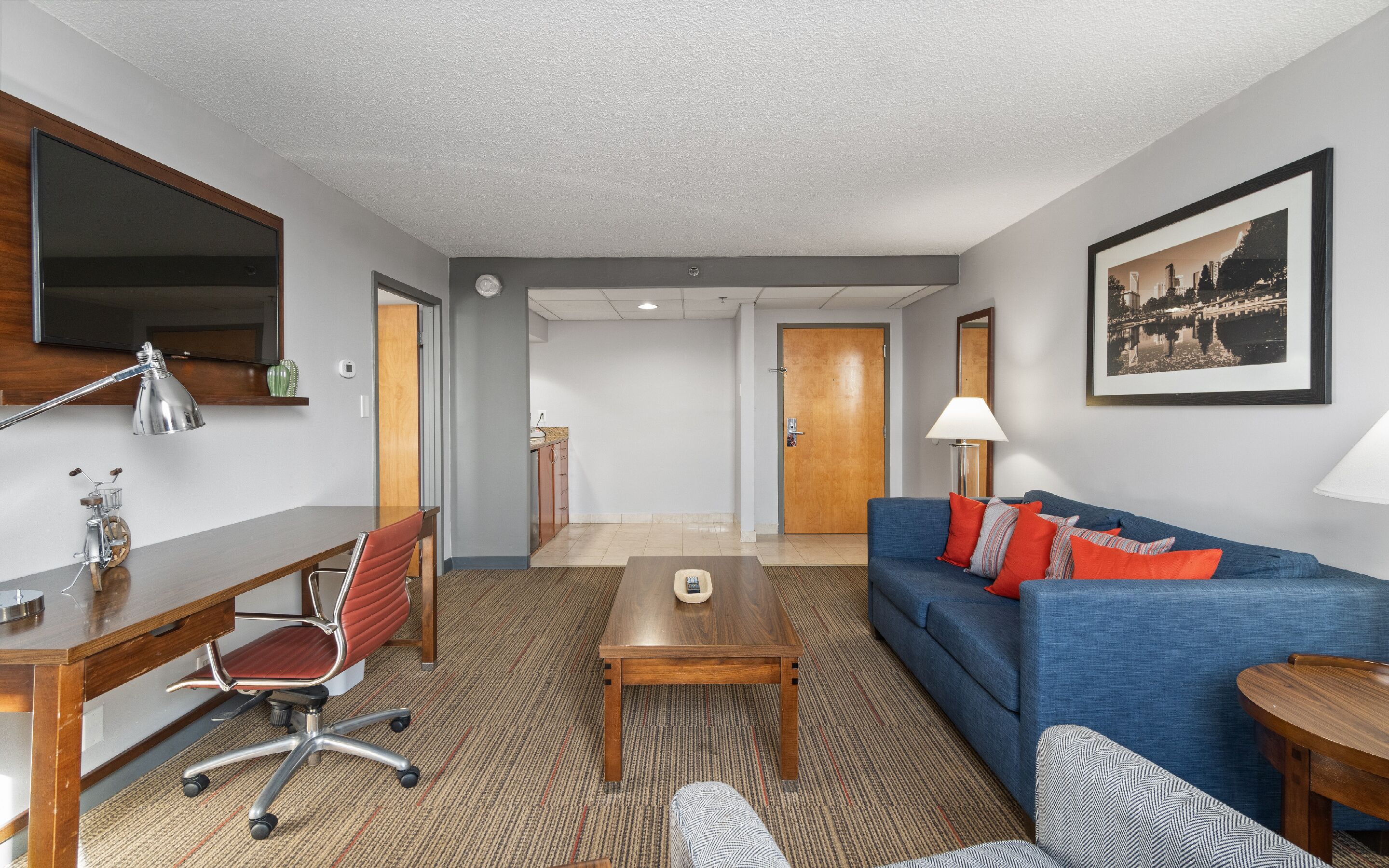 Ein modernes Hotelzimmer mit einem Holzbüro, einem blauen Sofa, einem Couchtisch und einem gerahmten Bild an der Wand.