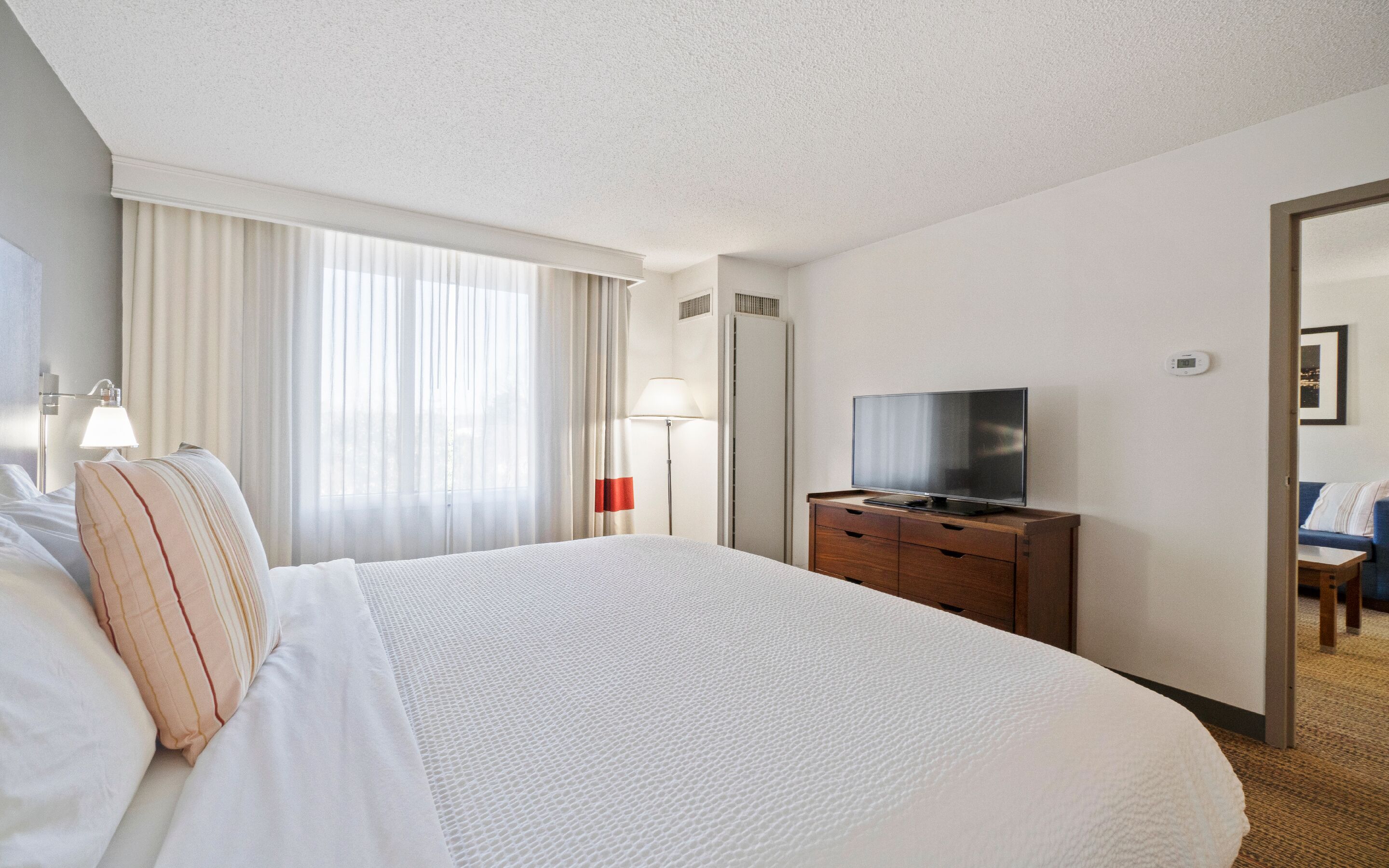 Una habitación de hotel con una cama grande, un televisor de pantalla plana, un aparador y un espejo.
