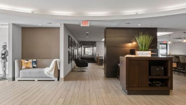 A modern hotel lobby with a wooden floor, a sofa with a throw blanket, a reception desk, and a plant. - 315@Loso Hotel (Charlotte)