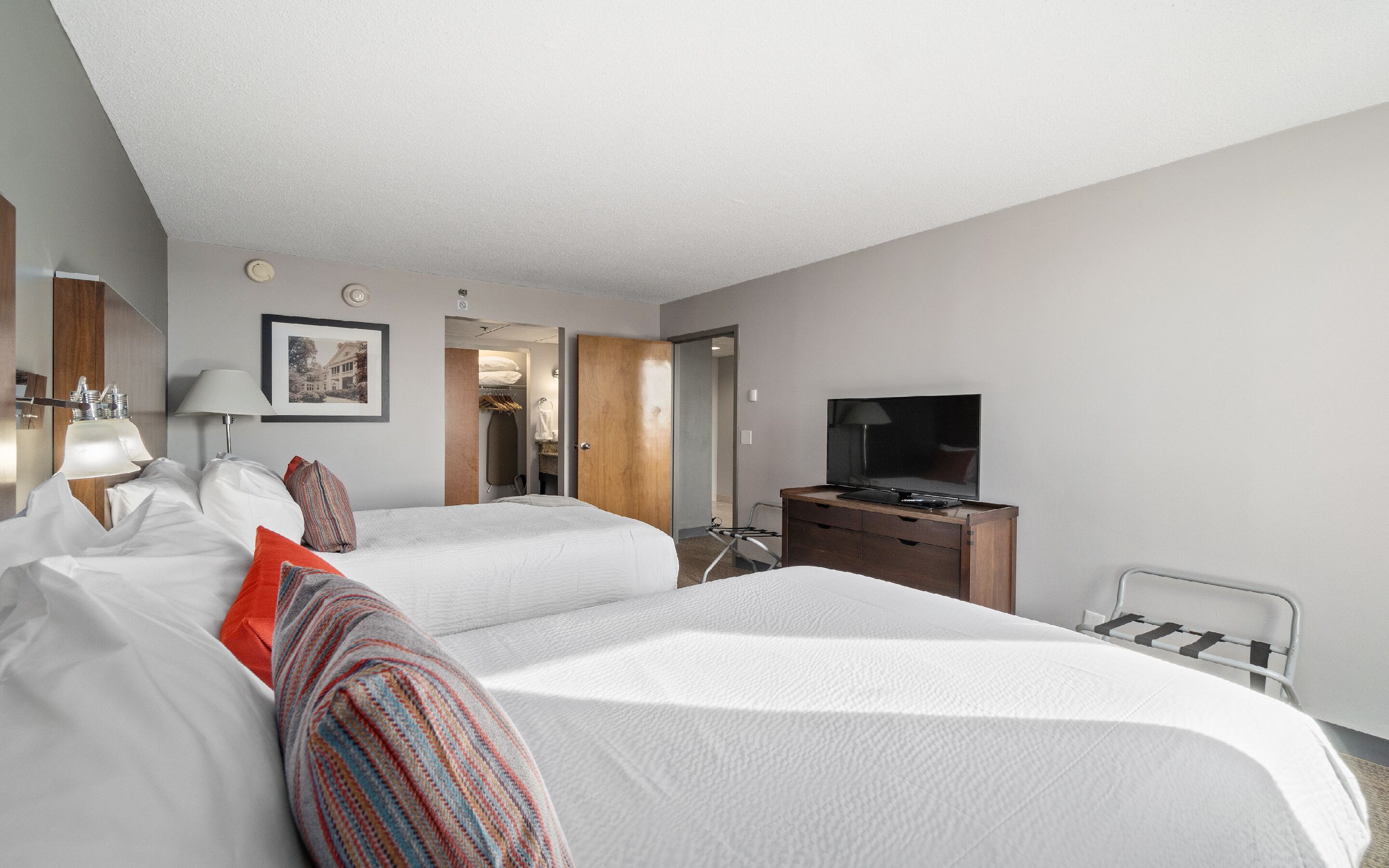 A hotel room with two beds, a TV, a desk, and a bathroom visible through an open door.