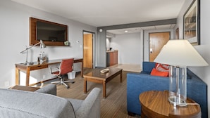 A hotel room with a wooden desk, a red office chair, a blue sofa, a small round table, a lamp, and a large mirror on the wall. - 315@Loso Hotel (Charlotte)