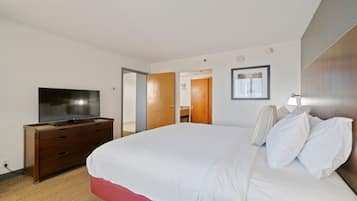 A hotel room with a bed, a TV on a wooden dresser, a bathroom visible through an open door, and a framed picture on the wall.