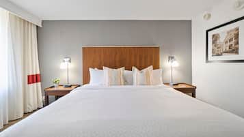 A hotel room with a large bed, two bedside tables, a wooden headboard, a framed picture on the wall, and a window with curtains.