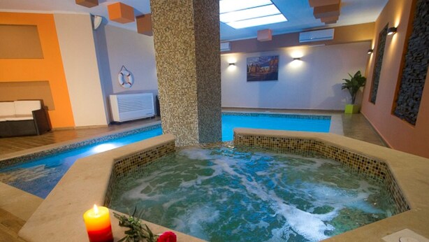Ein Whirlpool mit Kerze und Blumen, ein Schwimmbecken und ein Empfangsbereich mit einer Bank.
