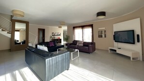 Ein geräumiges Wohnzimmer mit einer großen Couch, einer kleineren Couch, einem Couchtisch und einem flachbildfernseher, der an der Wand befestigt ist.