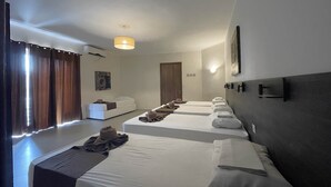 Ein Hotelzimmer mit drei Betten, einem Sofa, einer Deckenleuchte und einer Tür.