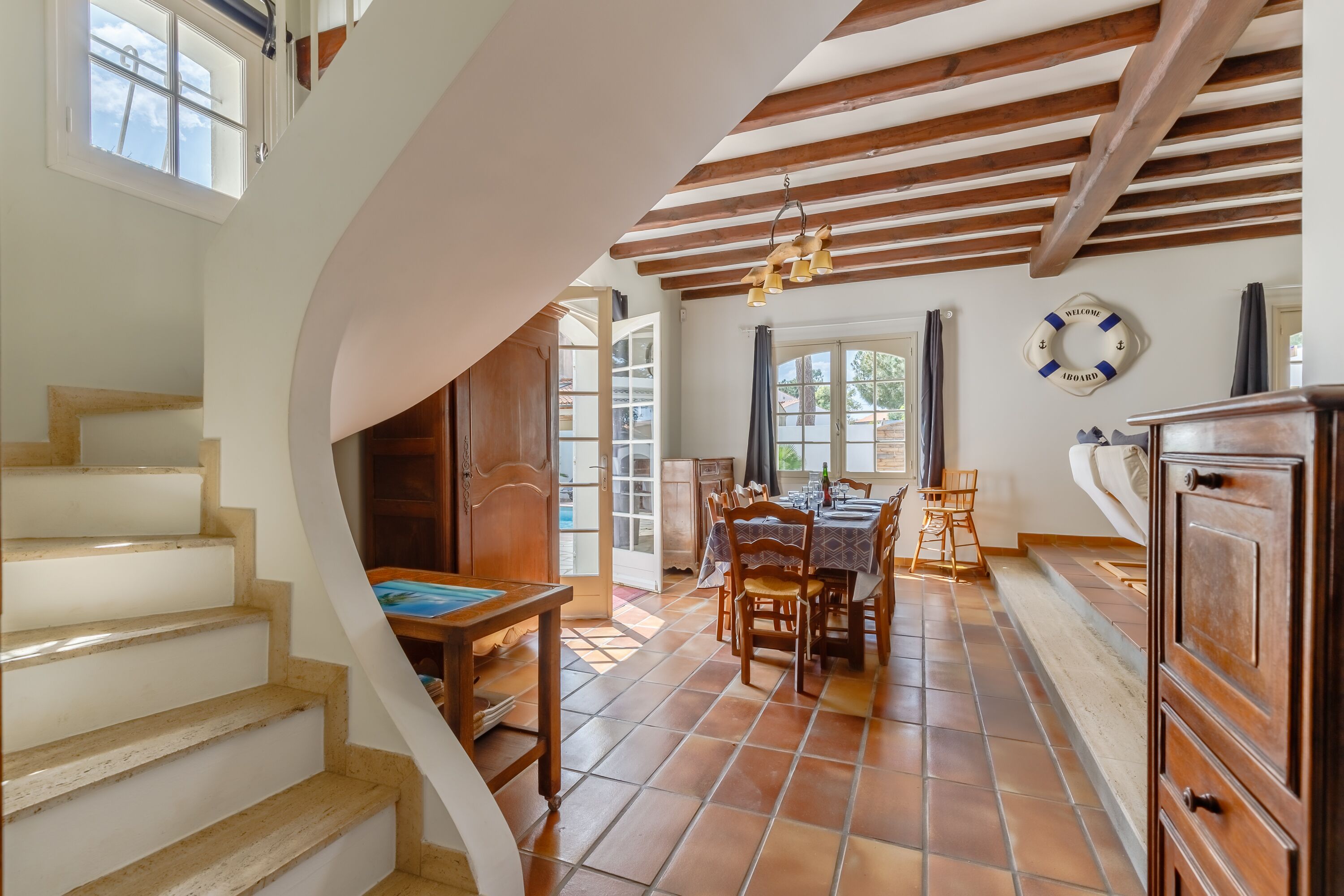 Un vaste espace dédié à la salle à manger, avec un escalier en bois, un sol carrelé et une vue sur l’extérieur.