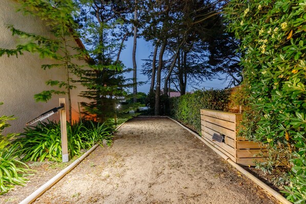 A pathway leading to a building with a wooden fence and dense foliage on one side. - Villa with SPA and private pool for 8 people (Bretignolles-sur-Mer)