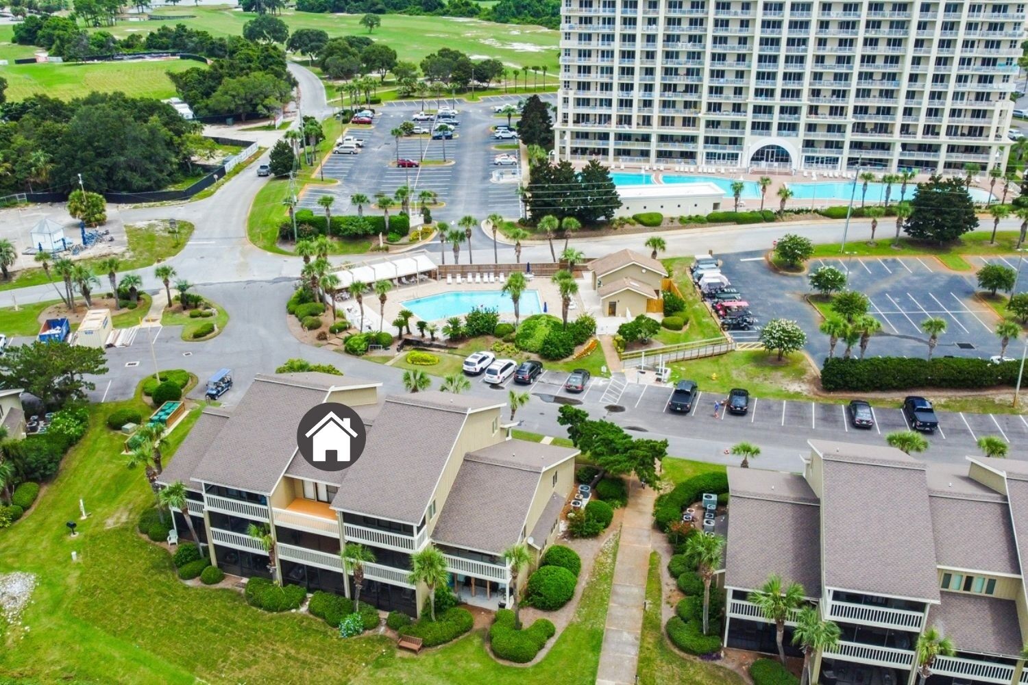 Vista aérea de un hotel con piscina, varios estacionamientos y zonas verdes circundantes.