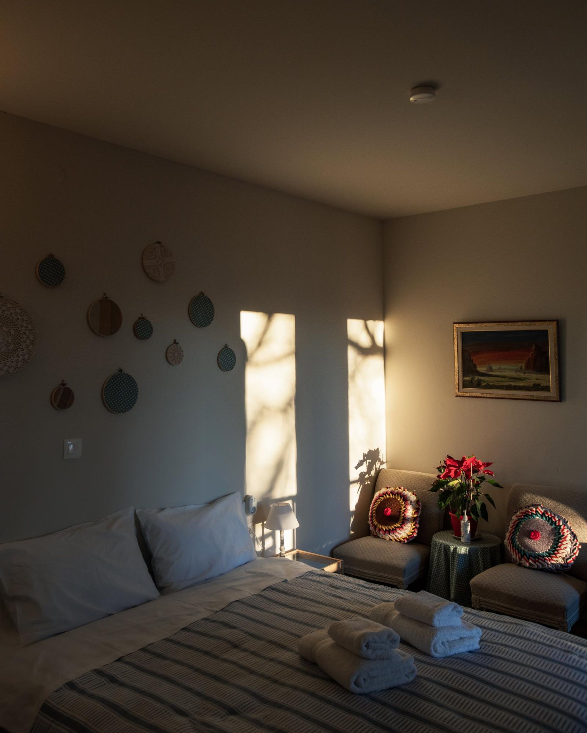 Una habitación de hotel con una cama, una silla, una mesita con una planta y un cuadro en la pared.
