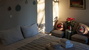 A hotel room with a bed, a chair, a small table with a plant, and a painting on the wall.
