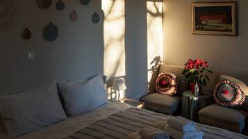 Una habitación de hotel con una cama, una silla, una mesita con una planta y un cuadro en la pared.