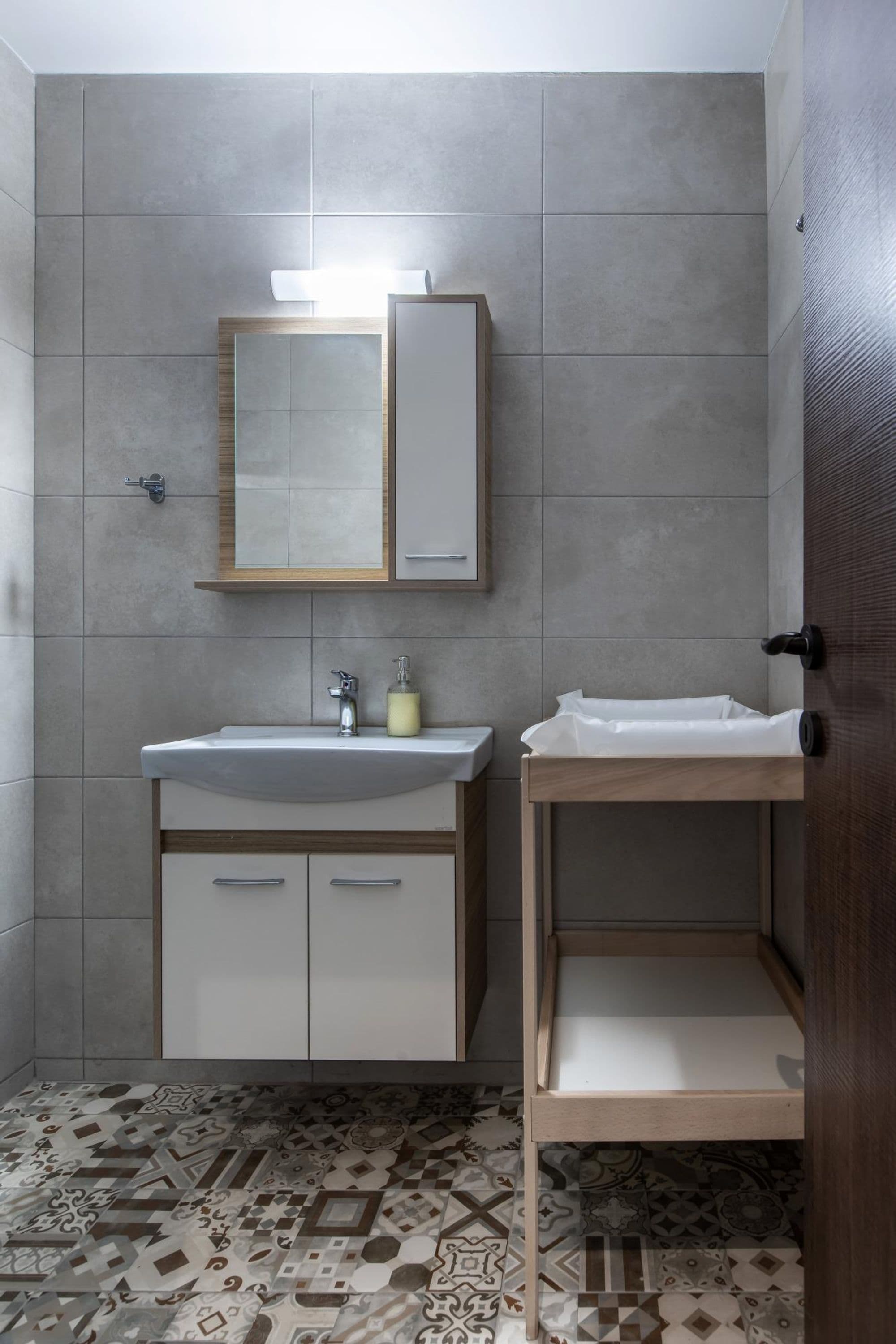 A bathroom with a sink, mirror, and a shelf unit.