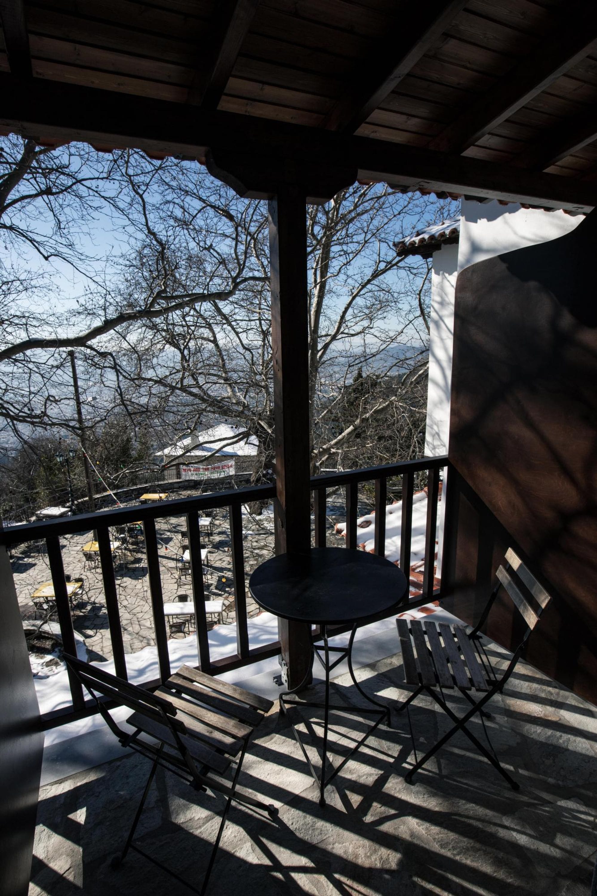 A covered outdoor area with a table and two chairs, a railing, and a view of a snowy landscape and buildings in the distance.