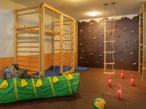 Uma academia de escalada com paredes de madeira para escalada, uma escada de corda e piso acolchoado.