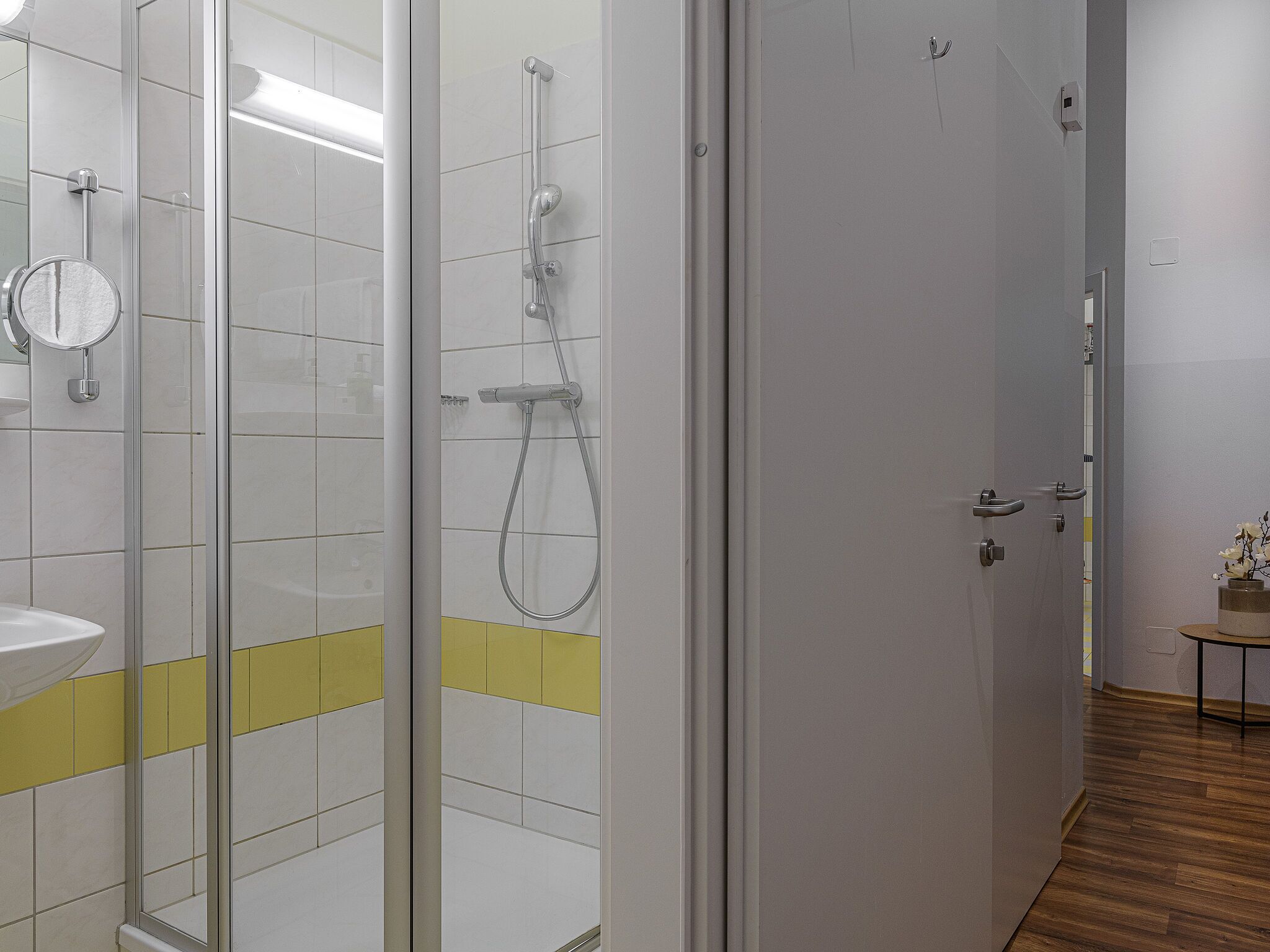 A modern bathroom with a glass shower enclosure, a white sink, and a yellow accent strip on the floor.