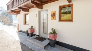 A building with a wooden balcony, a door, and two potted plants with a heart-shaped sign above the door. - Chalet in Hainzenberg Near Ski Slopes (Hainzenberg)
