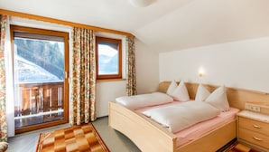 A bedroom with a wooden bed, a nightstand, a window with curtains, and a view of a snowy mountain. - Chalet in Hainzenberg Near Ski Slopes (Hainzenberg)