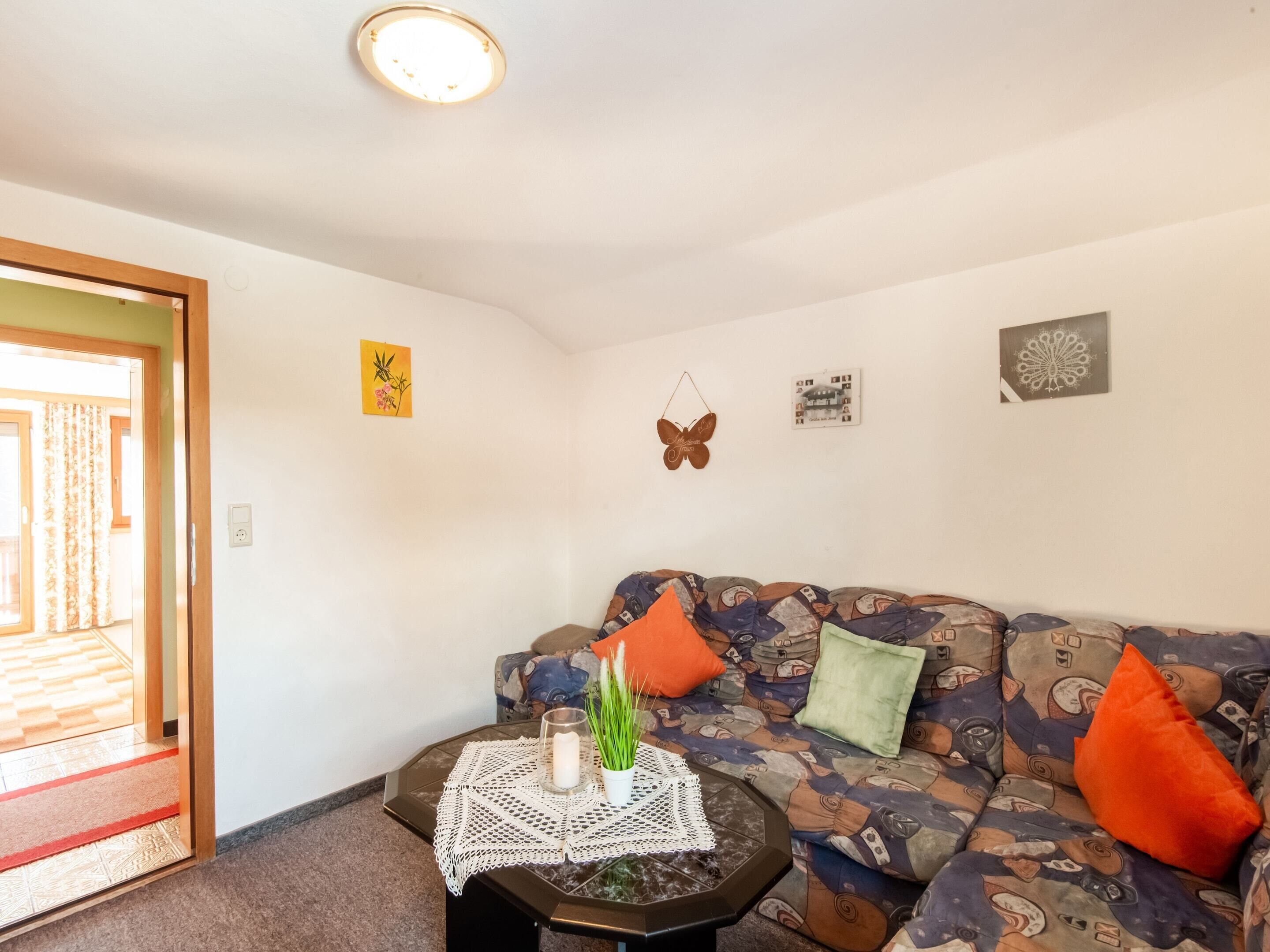 A living room with a patterned sofa, a small coffee table with a lace table runner, and a door leading to a balcony.