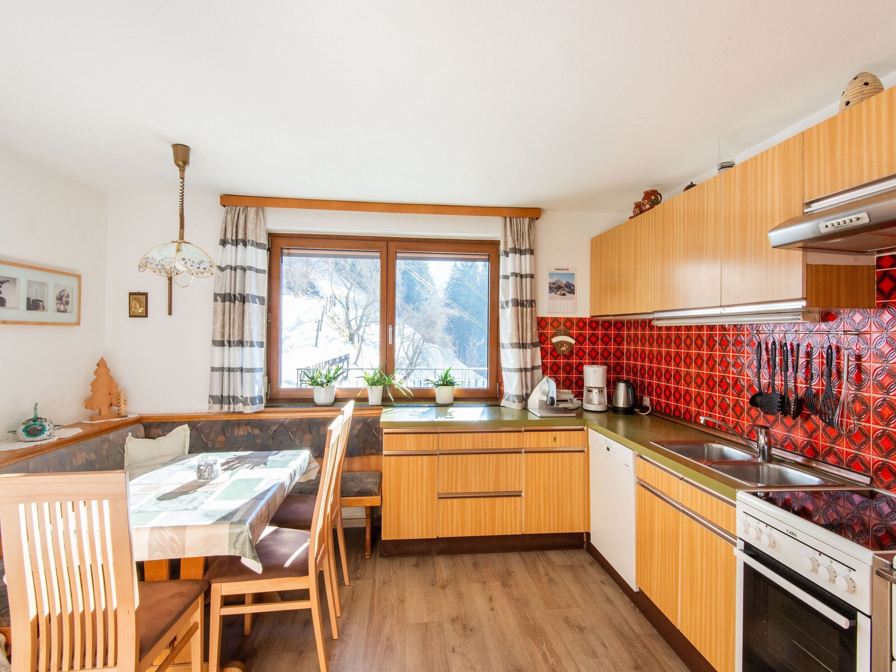 A compact kitchen with wooden cabinets, a dining area with a table and chairs, and a window with curtains.