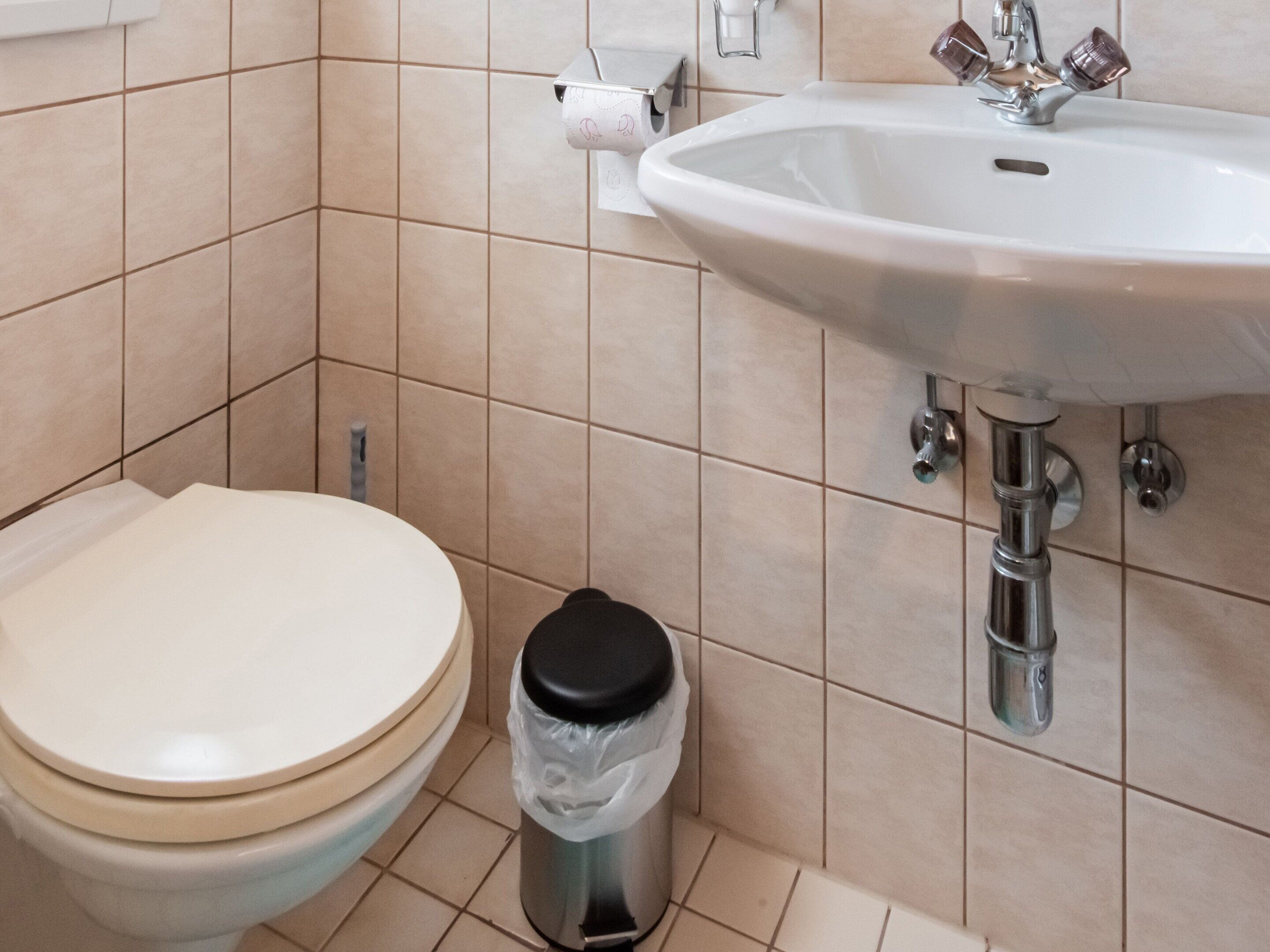 A bathroom with a toilet, a sink, and a trash bin.