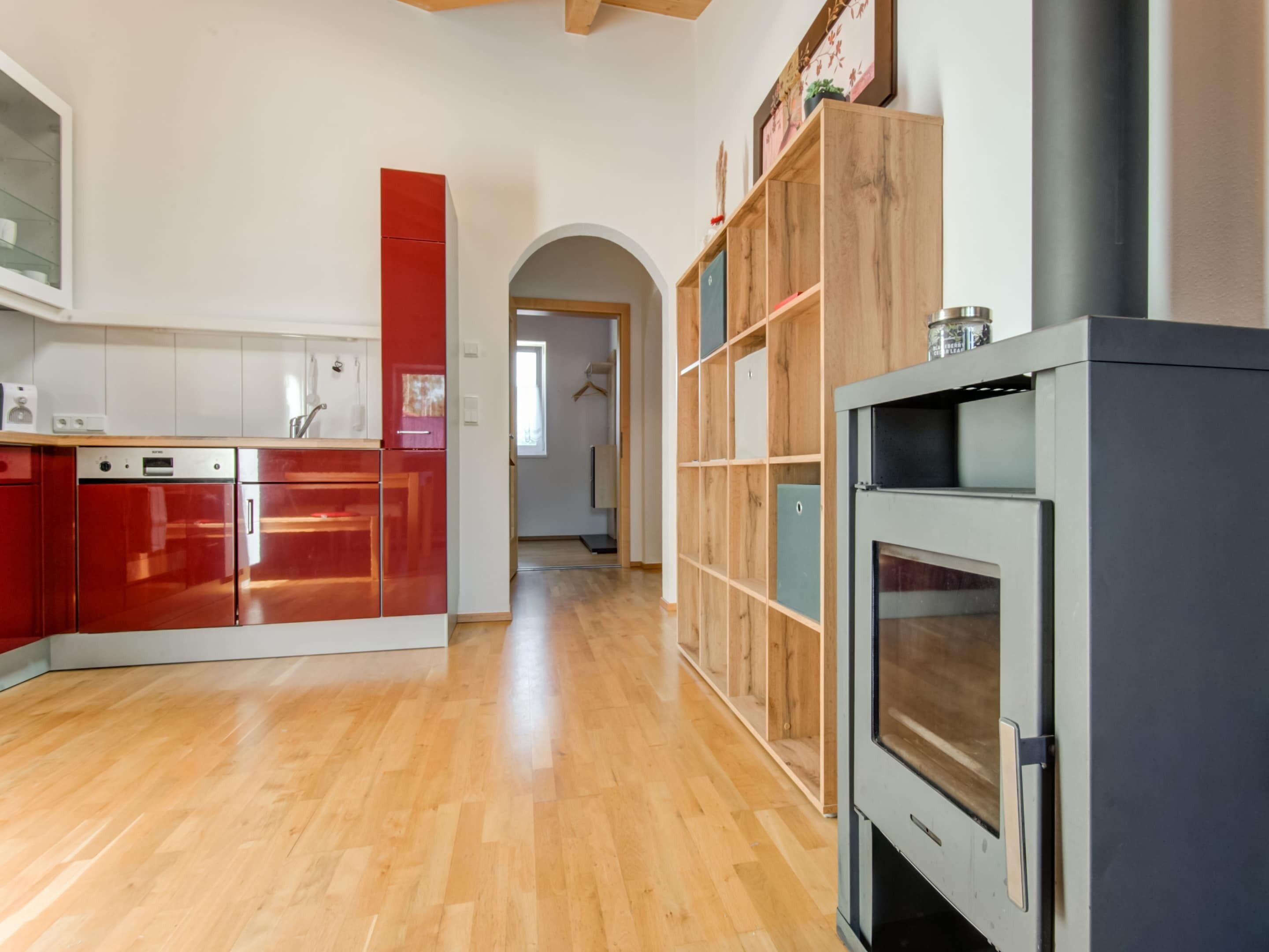 A modern kitchen with wooden flooring, a built-in oven, and red cabinetry.