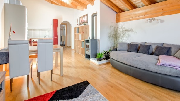 A modern living room with a wooden ceiling, a grey sofa, a dining area with chairs, and a kitchen in the background. - Cosy Flat in Westendorf in Tyrol (Westendorf)