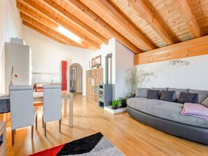 A modern living room with a wooden ceiling, a grey sofa, a dining area with chairs, and a kitchen in the background. - Cosy Flat in Westendorf in Tyrol (Westendorf)