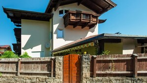 A two-story house with a balcony and a stone wall in front. - Cosy Flat in Westendorf in Tyrol (Westendorf)