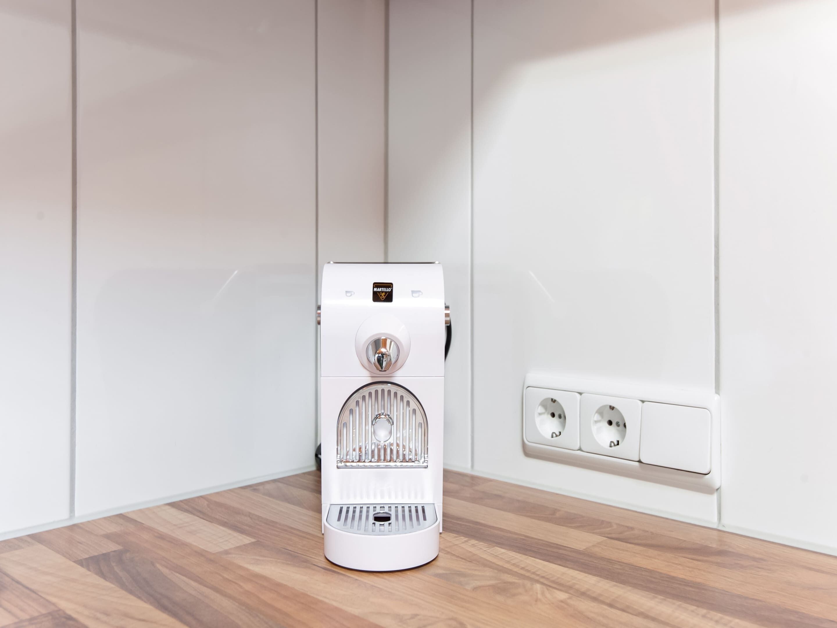 A white portable heater with a control panel and a power outlet on the wall.