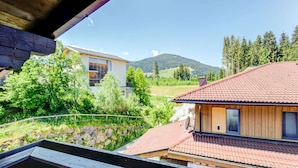 A modern house with a red-tiled roof, a wooden deck, and a view of a mountain and forest. - Cosy Flat in Westendorf in Tyrol (Westendorf)