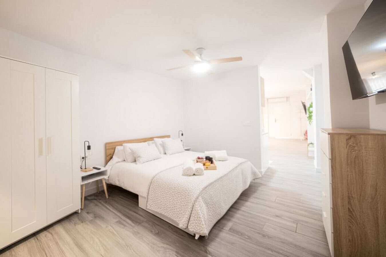 A modern bedroom with a wooden bed, white walls, and a ceiling fan.