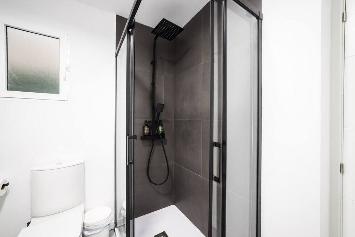 A modern bathroom with a glass-enclosed shower, a toilet, and a sink.