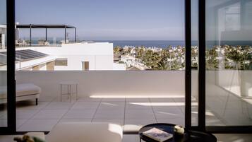 A modern room with a large window overlooking a coastal view, featuring a sofa, a small table, and a glass railing.